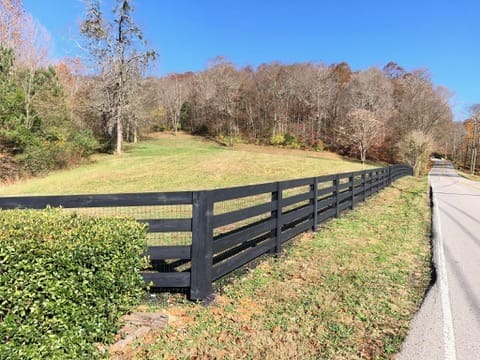 Black wooden fence along a grassy yard with trees in the background, showcasing a stylish and durable fencing solution for homeowners in Middle Tennessee.