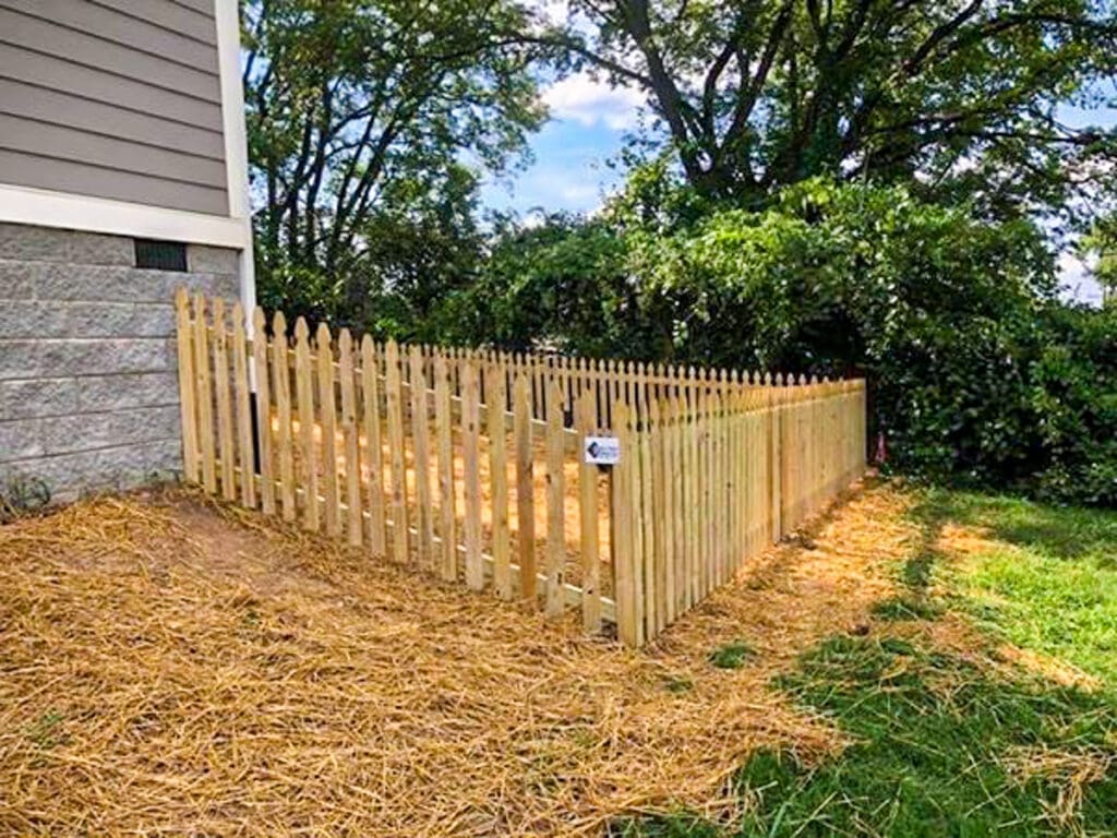 Wooden picket fence enclosing a backyard area, showcasing a recent installation by Home Deck and Fence in Middle Tennessee, with a backdrop of trees and a clear sky.