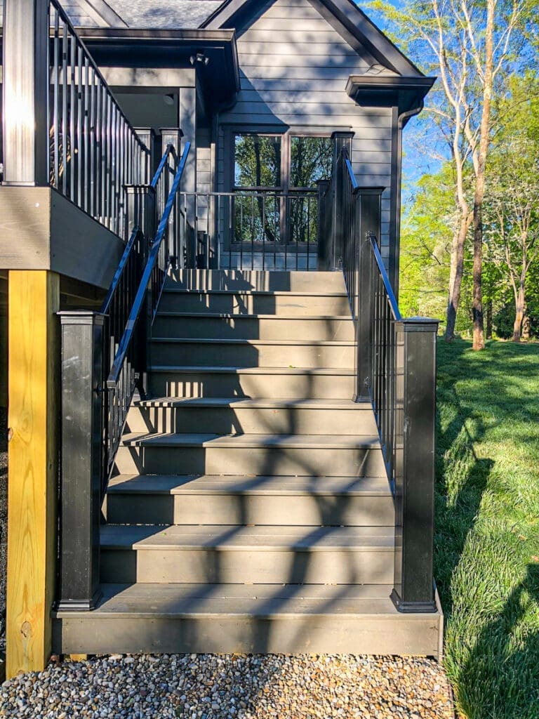Staircase leading to a modern home deck with black railings, surrounded by green grass and trees, illustrating outdoor structure solutions by Home Deck and Fence Co. in Middle Tennessee.