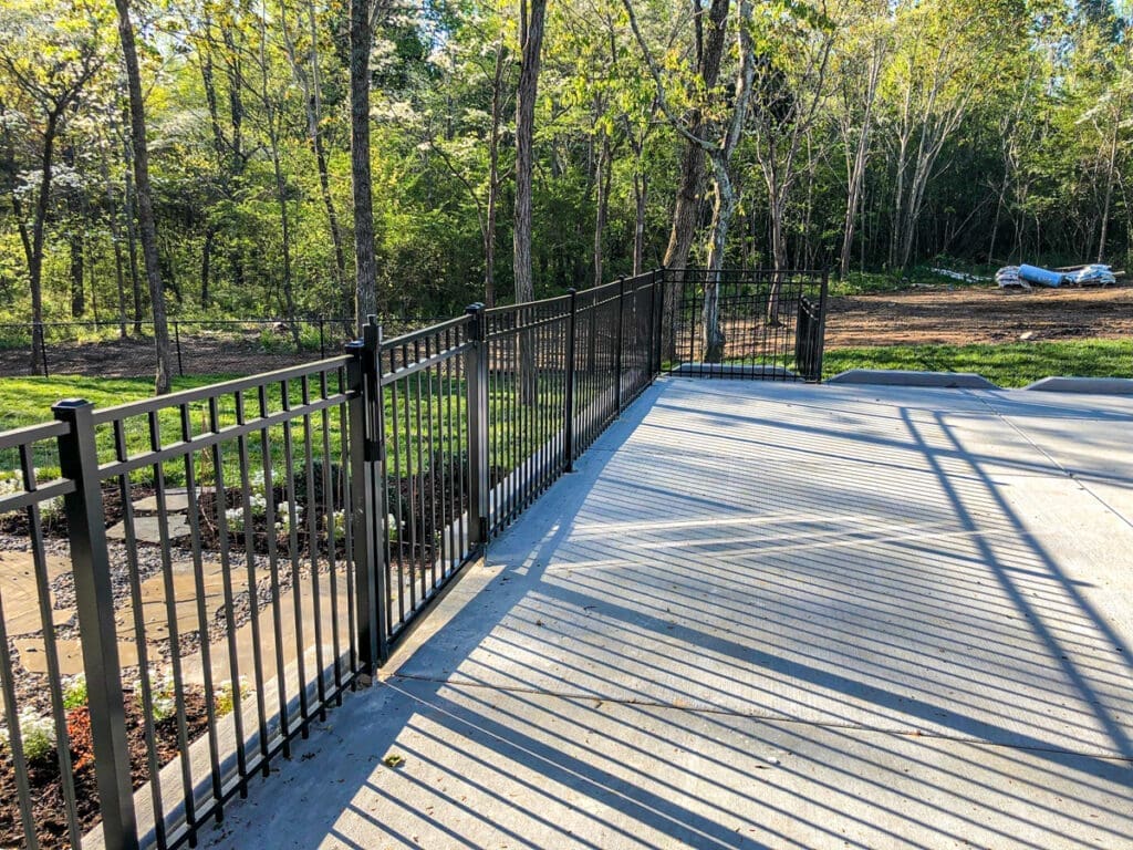 Black metal fence surrounding a concrete deck in a wooded area, showcasing custom outdoor structures by Home Deck & Fence Co. for enhanced safety and style in Middle Tennessee.