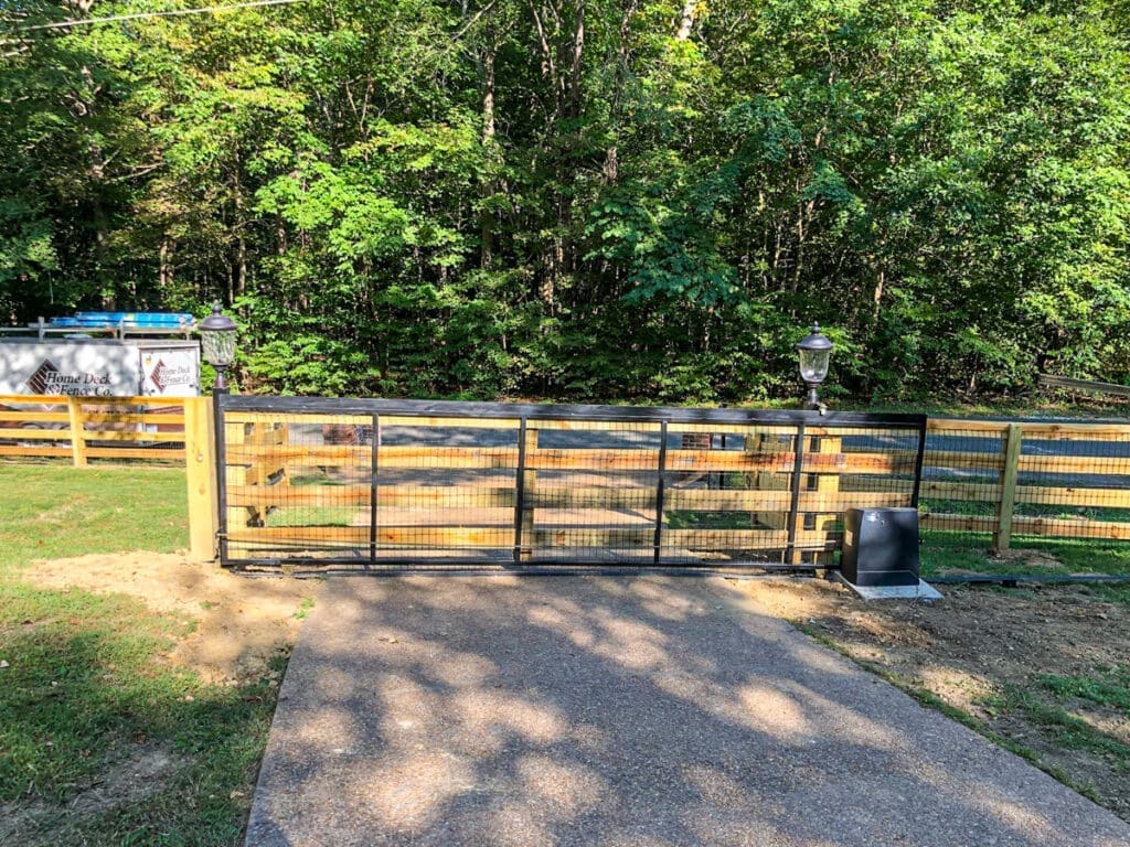 Pet-friendly fence gate with wooden posts and black metal mesh, surrounded by greenery, featuring Home Deck and Fence Co. branding.