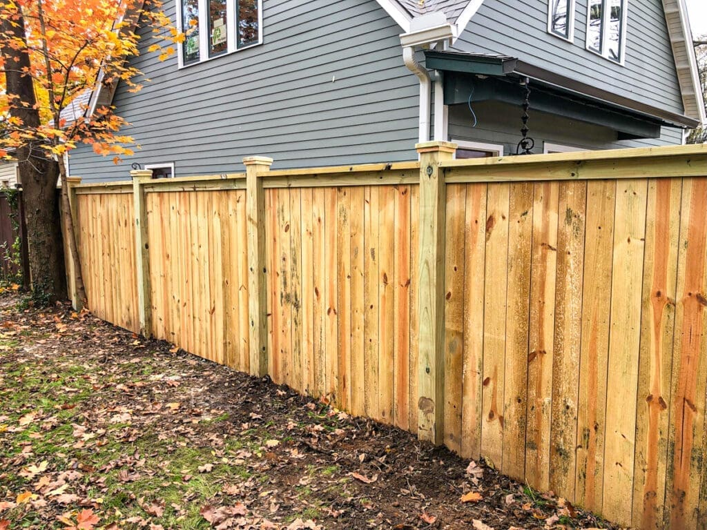 New wooden privacy fence installed in a residential yard, showcasing sturdy construction and natural wood finish, surrounded by autumn foliage and a gray house exterior, reflecting Home Deck and Fence's quality craftsmanship in Middle Tennessee.