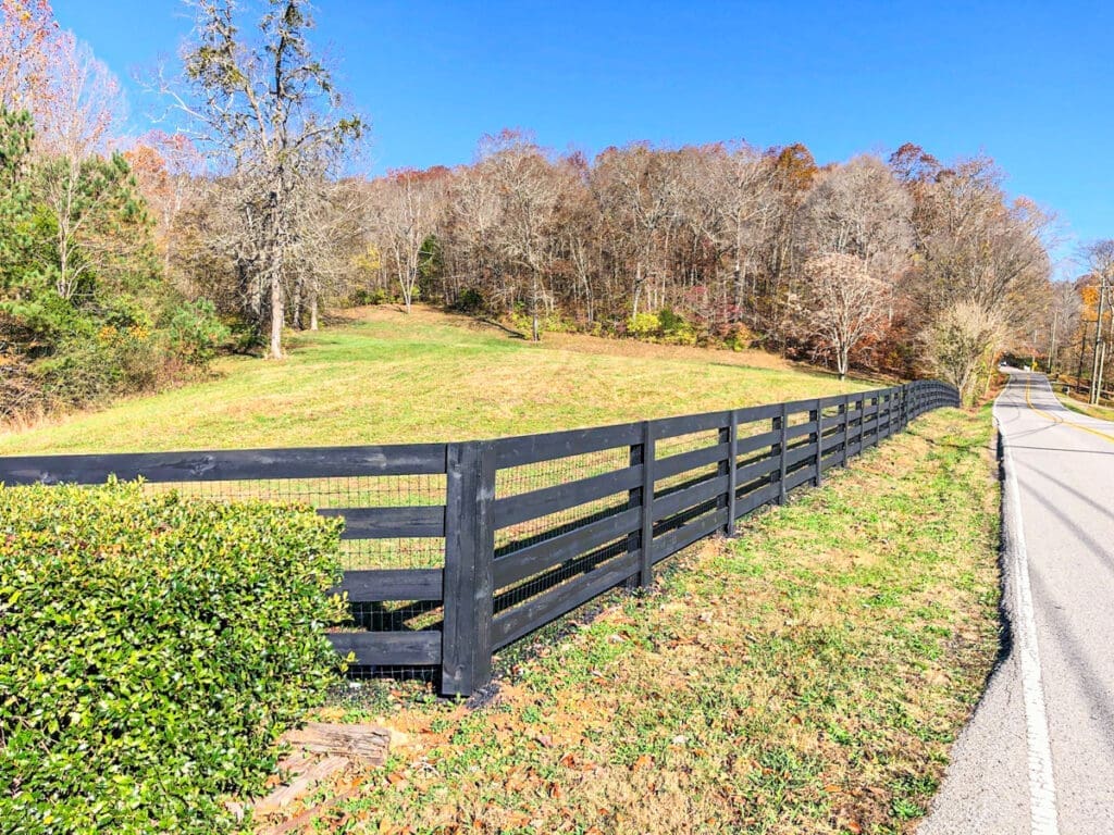 Black wooden fence along a grassy field in Middle Tennessee, showcasing professional fence installation amidst autumn foliage.
