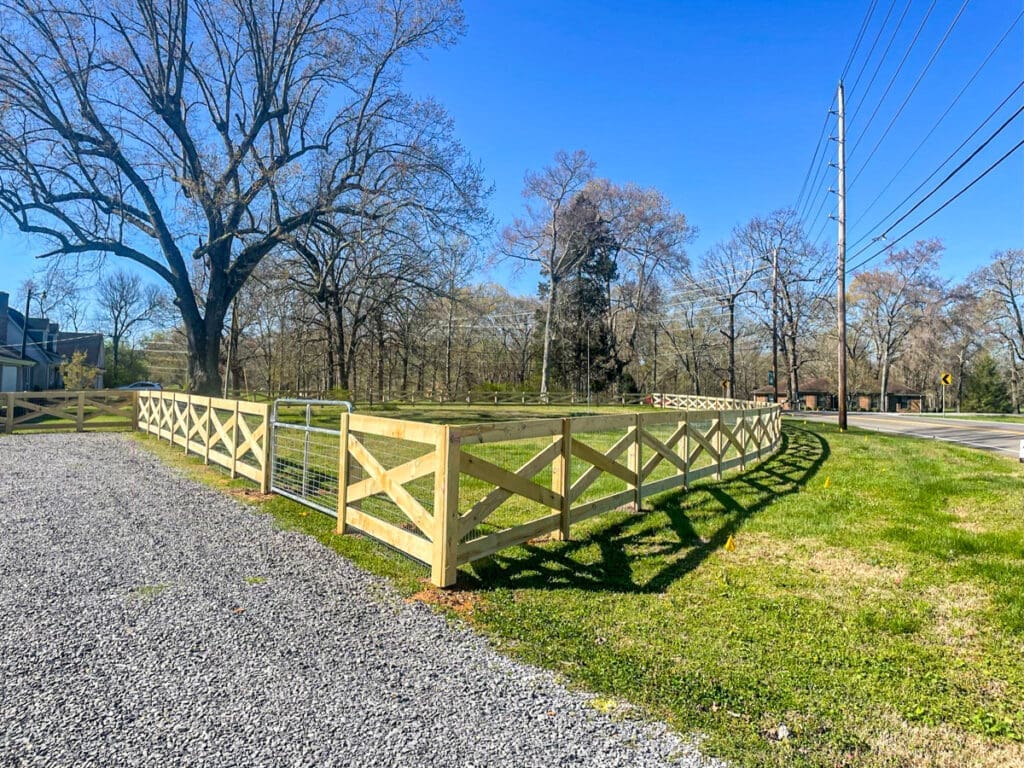 New wooden fence with X-bracing and gate, surrounding a grassy area near a residential property in Dickson County, Tennessee, showcasing outdoor design and fencing solutions by Home Deck and Fence.