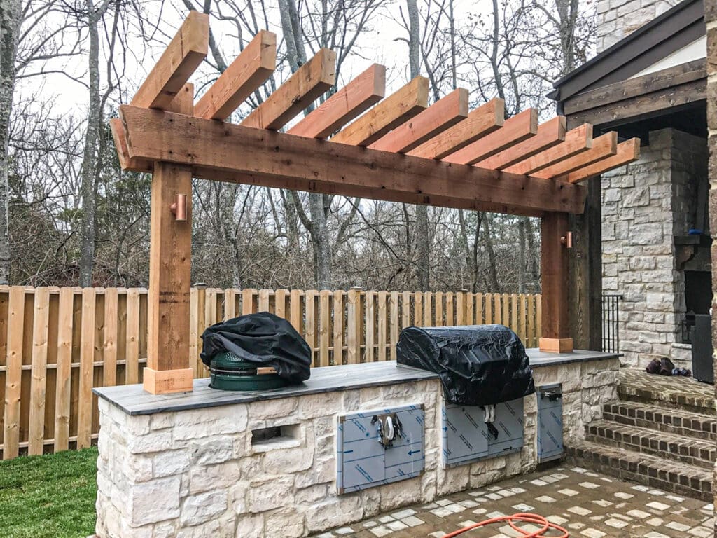 Custom outdoor pergola structure with stone base and grill area, surrounded by wooden fencing in a residential setting, showcasing craftsmanship by Home Deck & Fence Co. in Dickson County, TN.