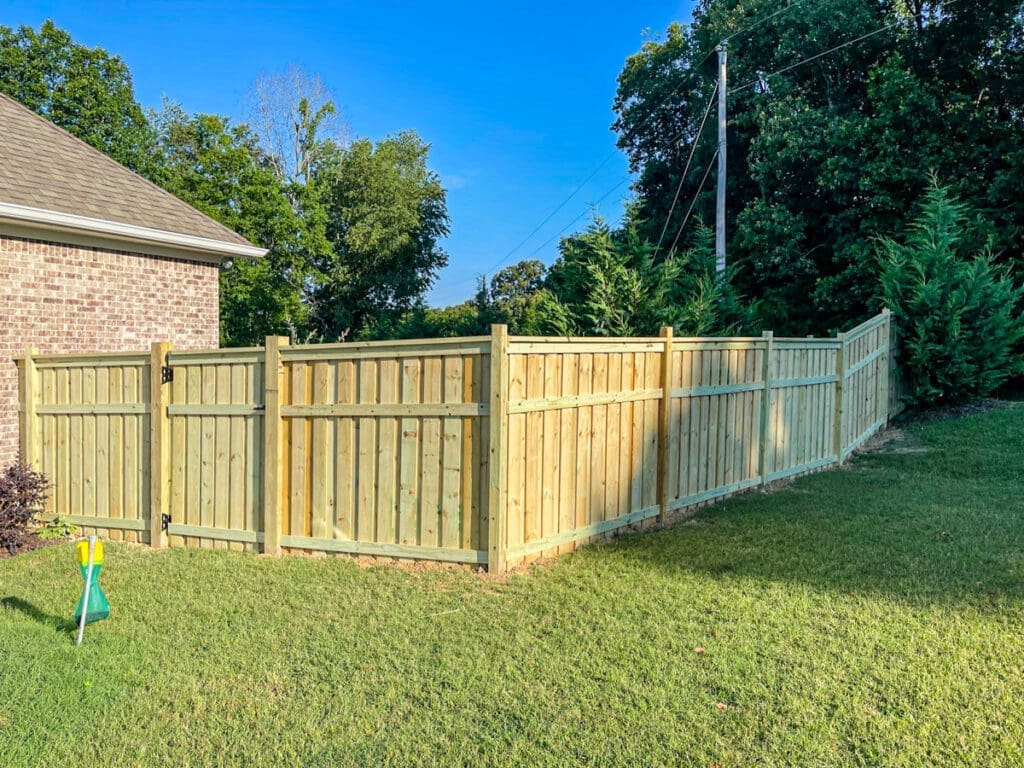 New wooden privacy fence enclosing a yard, showcasing sturdy construction and a natural finish, surrounded by green grass and trees in Middle Tennessee.