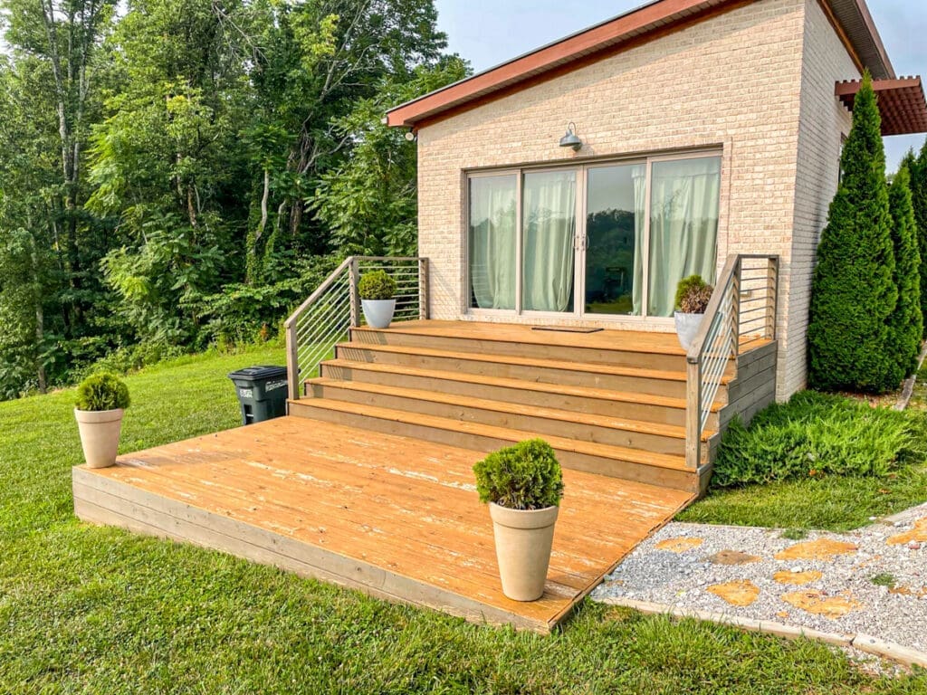 Wooden deck with steps leading to a modern home, surrounded by greenery, showcasing professional craftsmanship in deck construction for outdoor living in Middle Tennessee.