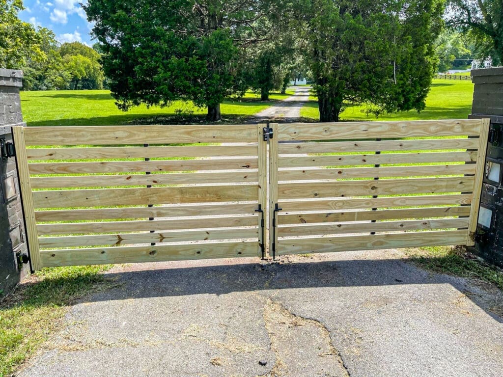 Wooden slatted gate opening to a grassy pathway, showcasing a pet-friendly fencing solution in Middle Tennessee.