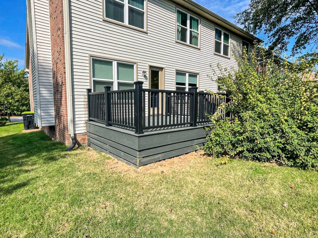 Backyard deck installation by Home Deck & Fence, featuring black railing and steps, adjacent to a brick home in Dickson County, TN, surrounded by greenery.