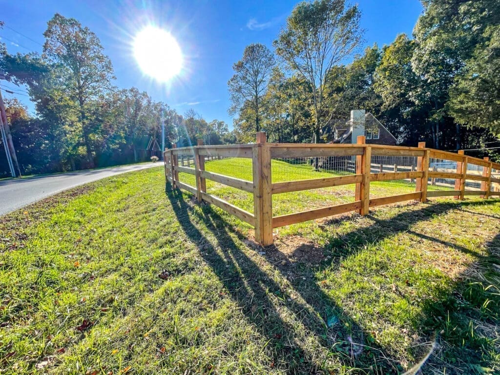 Wooden fence enclosing a grassy area with sunlight shining down, showcasing professional fence installation by Home Deck & Fence in Middle Tennessee.