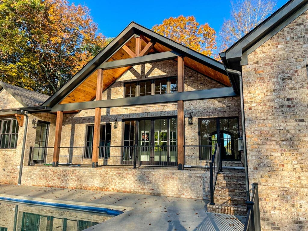 Custom outdoor home design featuring a modern brick house with wooden accents, large windows, and a spacious patio area, surrounded by autumn foliage in Middle Tennessee.