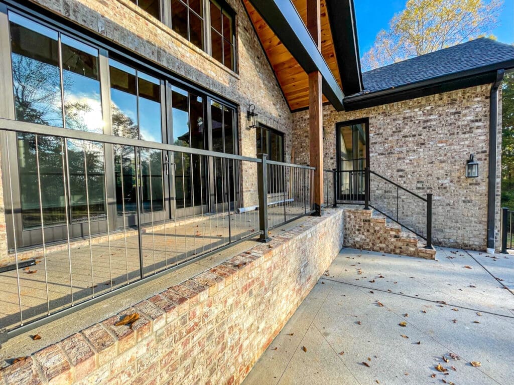 Modern outdoor deck with metal railing and brick steps, featuring large windows and wooden accents, enhancing home aesthetics in Middle Tennessee.