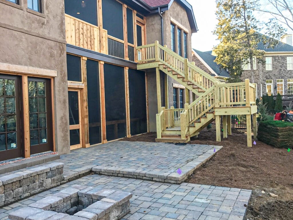 Custom wooden deck with stairs and screened-in porch, surrounded by paver patio and landscaping, showcasing outdoor construction services by Home Deck & Fence Co. in Dickson County, Tennessee.