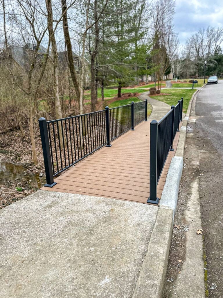 Custom wooden walkway with black railings in Middle Tennessee, surrounded by trees and grass, enhancing outdoor space safety and style.