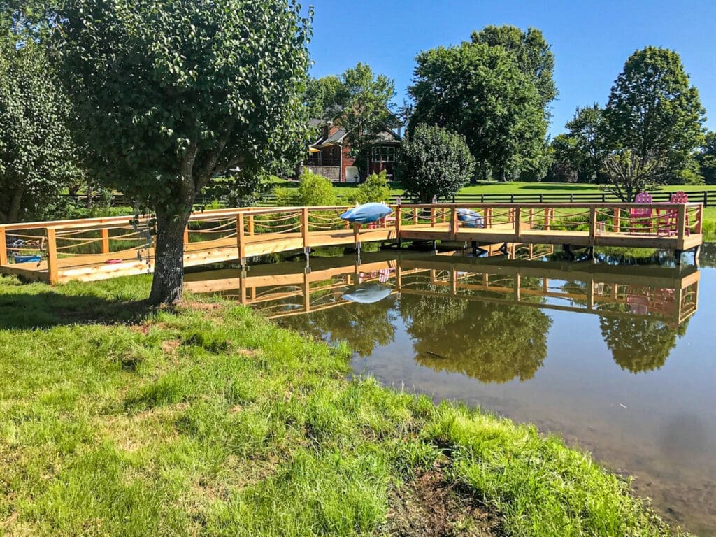 Custom wooden walkway over water with reflections, surrounded by greenery and trees, enhancing outdoor space in Middle Tennessee.
