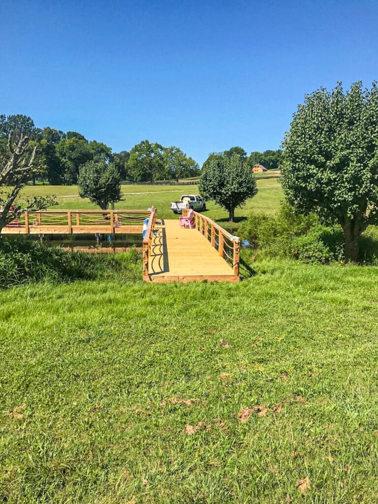 Custom wooden bridge over grassy area, surrounded by trees, showcasing outdoor craftsmanship by Home Deck and Fence in Dickson, TN.