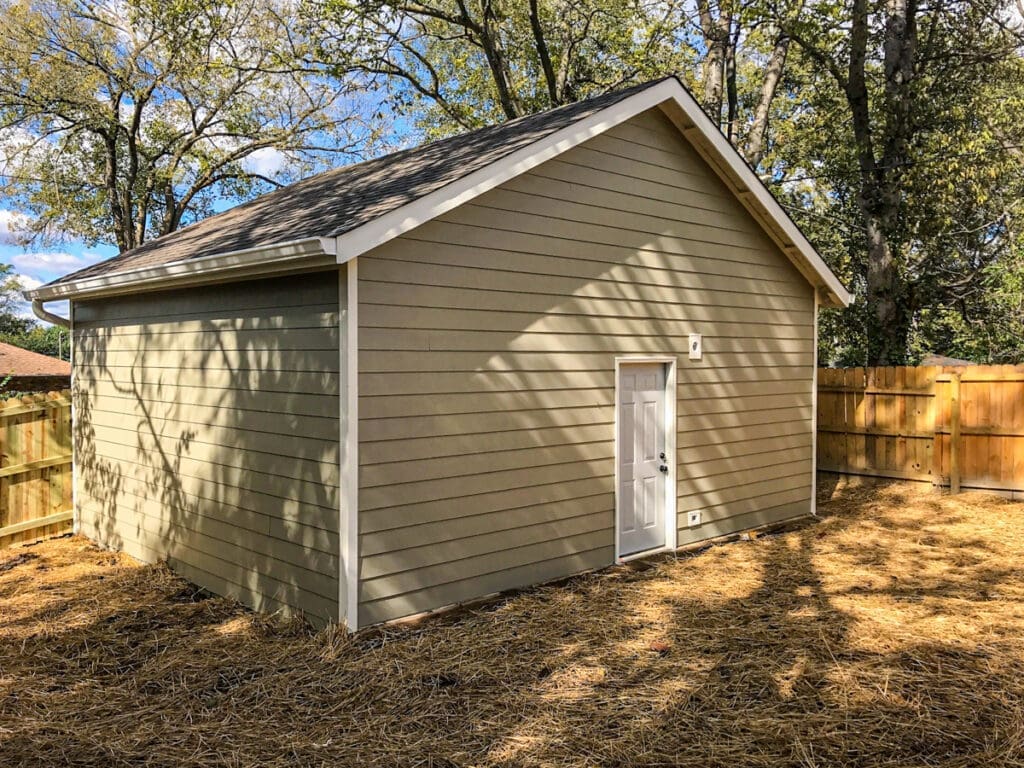 Custom-built storage shed in Middle Tennessee, featuring a light-colored exterior and a white door, surrounded by a wooden fence and natural landscaping.