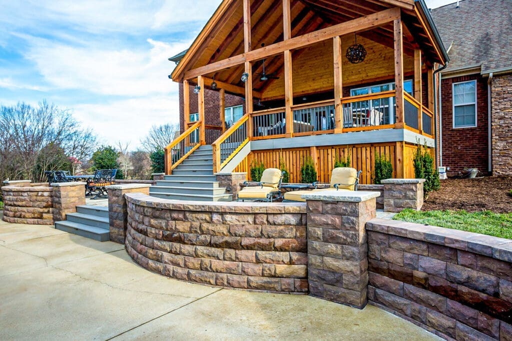 Deck and patio area featuring a wooden structure with a gabled roof, stone seating walls, and landscaped surroundings, showcasing professional craftsmanship by Home Deck & Fence Co. in Dickson County, Tennessee.