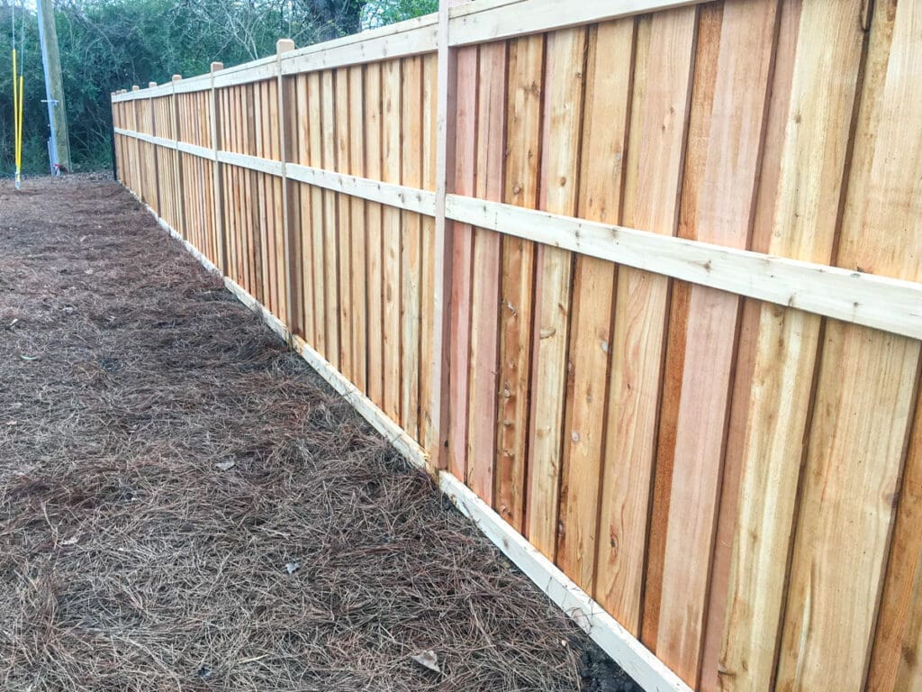 Newly installed wooden fence in Middle Tennessee, showcasing vertical wooden planks with natural wood tones, surrounded by pine straw, emphasizing quality fencing solutions for homeowners.