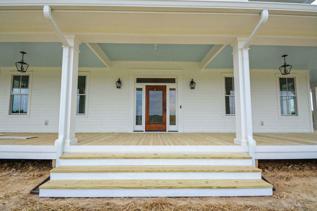 Newly constructed white porch with wooden steps, featuring decorative lanterns and large windows, showcasing outdoor living space by Home Deck and Fence Co. in Dickson County, Tennessee.