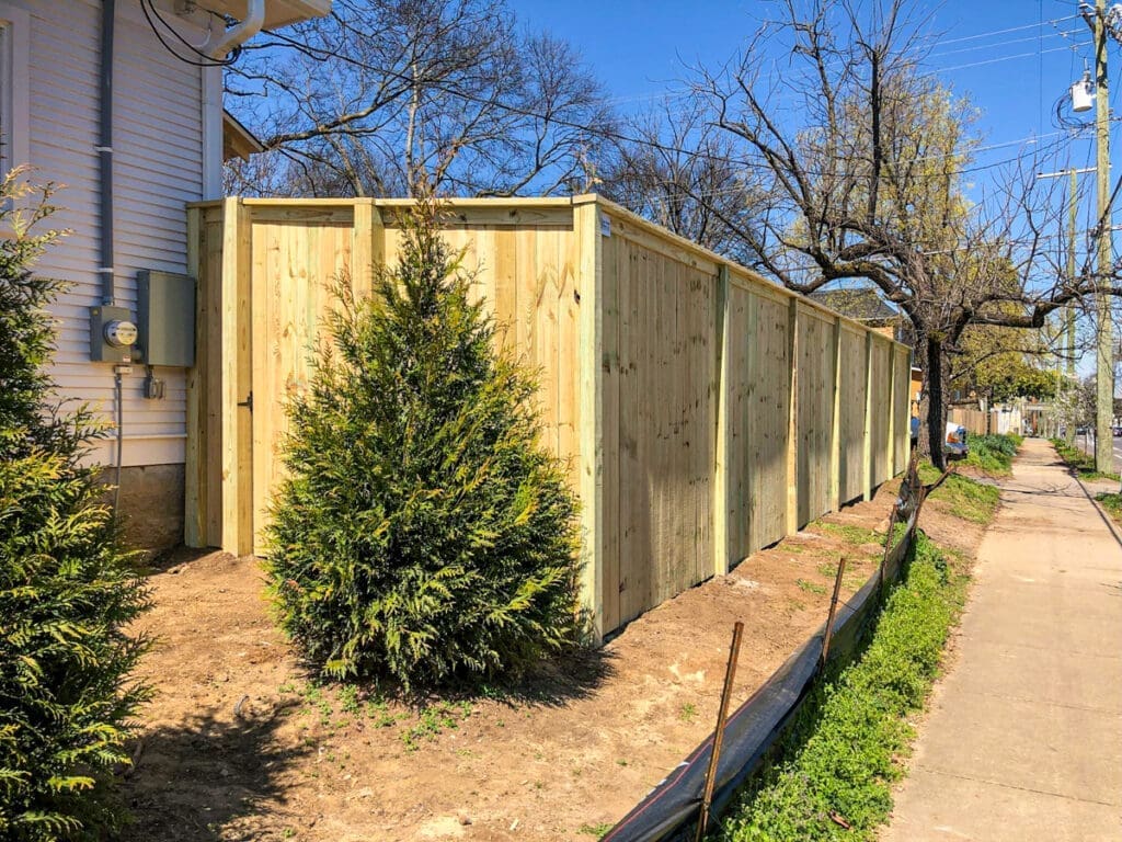 New wooden fence installed beside a house in Middle Tennessee, featuring green shrubs and a clear blue sky, emphasizing privacy and security for homeowners.