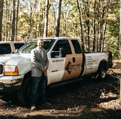 Man in a suit standing next to a Home Deck and Fence Company pickup truck in a wooded area, showcasing the company’s branding and commitment to quality outdoor services in Middle Tennessee.