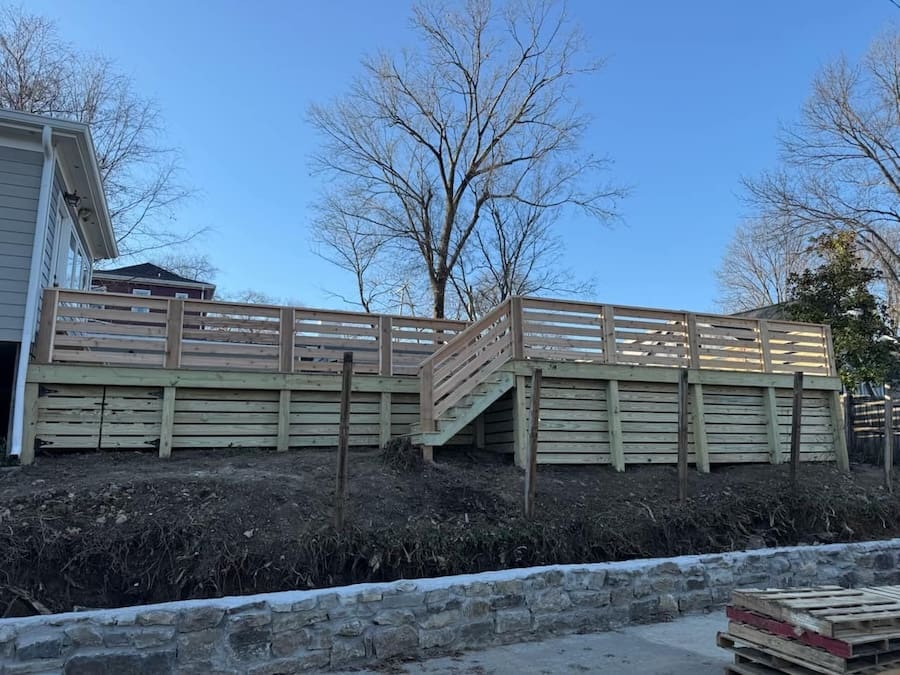 Multi-tiered wooden deck with staircase, designed for outdoor entertainment and storage, set against a clear blue sky in a sloped backyard.