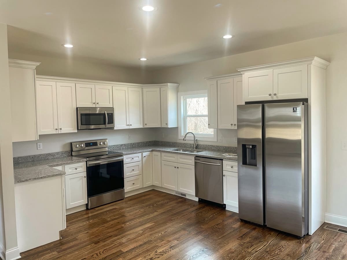 Modern kitchen with stainless steel appliances, white cabinetry, granite countertops, and hardwood flooring, showcasing a functional design ideal for spec homes by HDF Builders in Middle Tennessee.