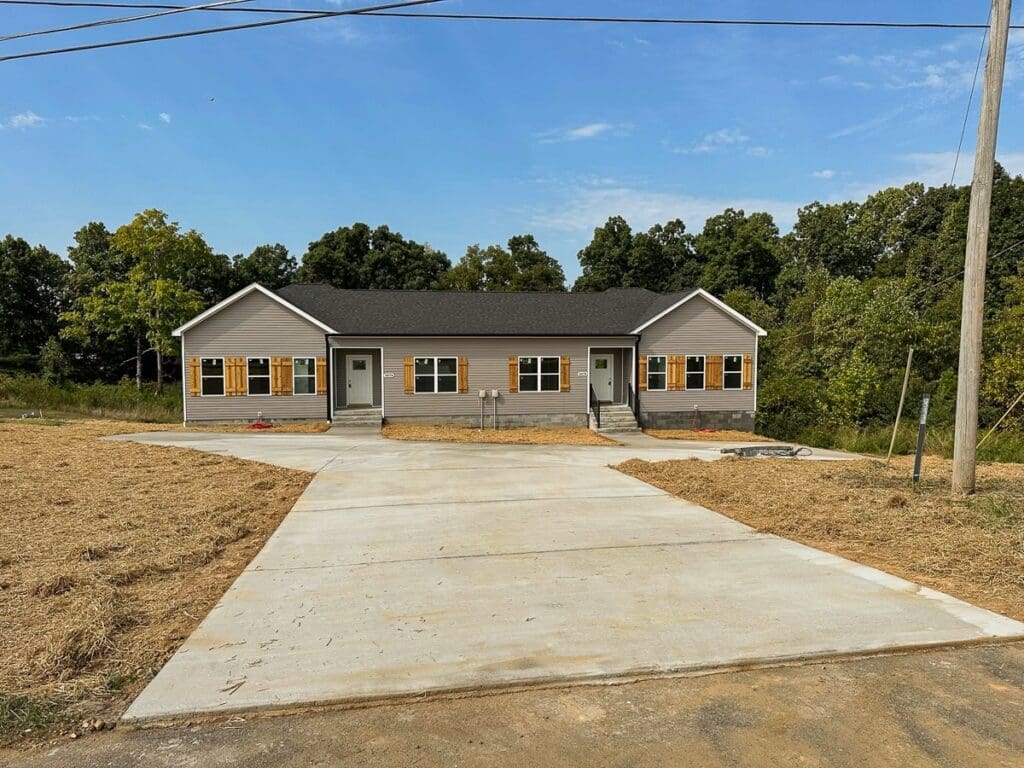 Duplex home built by HDF Builders in Middle Tennessee, featuring a modern exterior with gray siding, orange shutters, and a concrete driveway, surrounded by greenery.
