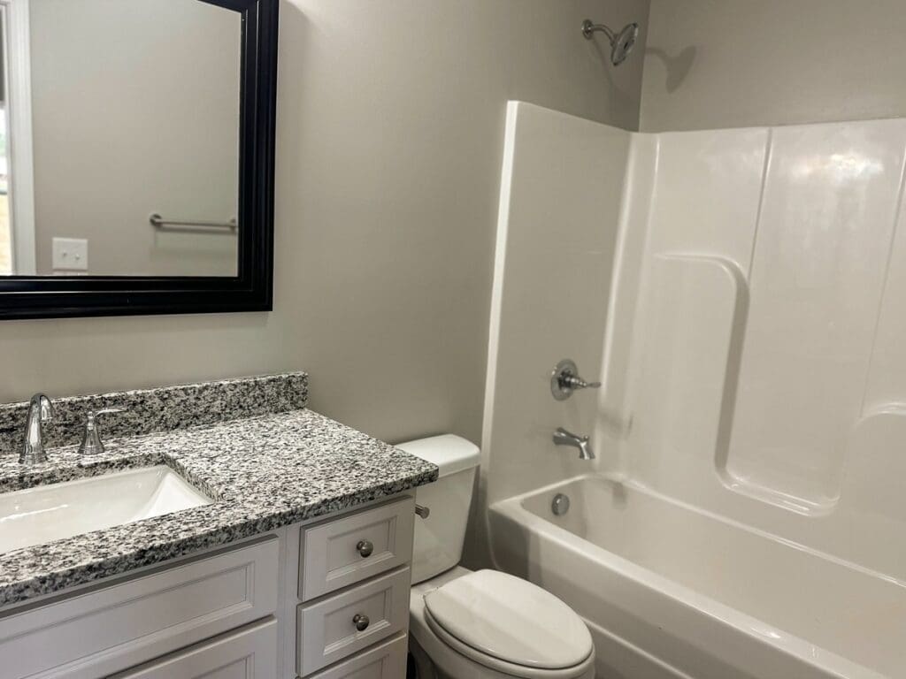 Modern bathroom featuring a granite countertop sink, white cabinetry, and a bathtub with shower, emphasizing low-maintenance finishes and contemporary design for investment properties in Middle Tennessee.
