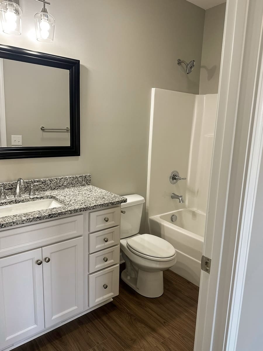 Modern bathroom featuring granite countertop, white cabinetry, mirror with black frame, shower/tub combination, and wood-like flooring, illustrating HDF Builders' commitment to quality and investor-friendly design in duplex construction.