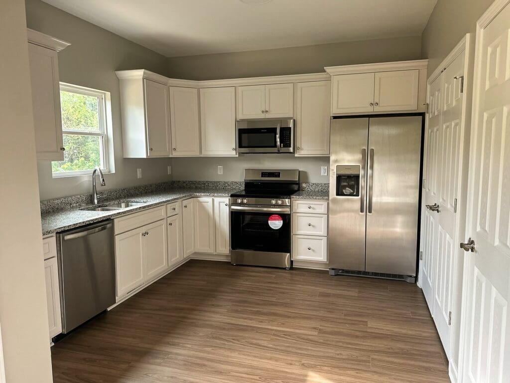 Modern kitchen interior featuring white cabinetry, stainless steel appliances, granite countertops, and a window providing natural light, showcasing HDF Builders' quality in custom home construction.
