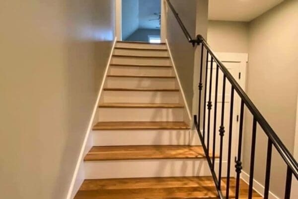 Staircase with wooden steps and black railing leading to a well-lit hallway in a custom-built home by HDF Builders in Middle Tennessee.
