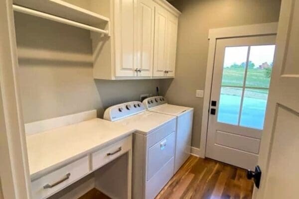Laundry room with white cabinetry, countertop, and washing machines, featuring a door leading to an outdoor view, showcasing custom home design by HDF Builders in Middle Tennessee.