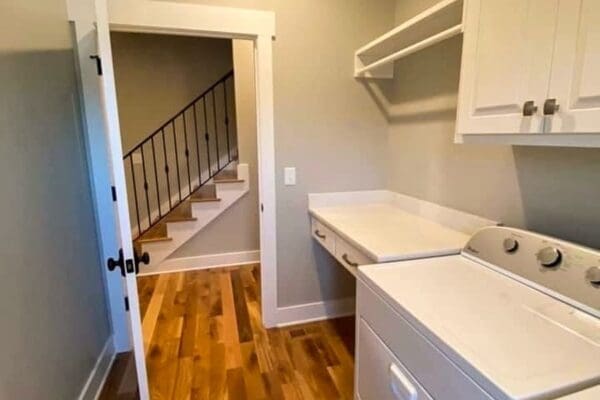Laundry room featuring a washing machine and countertop, leading to a staircase with black railing, emphasizing custom home design by HDF Builders in Middle Tennessee.