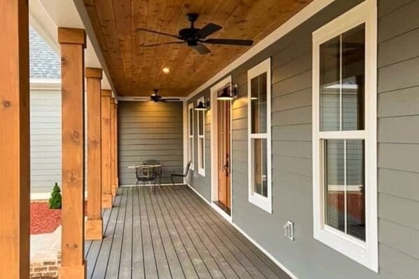 Covered front porch of a custom home by HDF Builders, featuring wooden beams, ceiling fan, and modern gray siding with white trim, showcasing inviting outdoor space.
