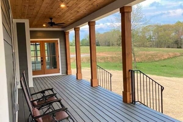 Front porch of a custom home by HDF Builders in Middle Tennessee, featuring wooden beams, a ceiling fan, and rocking chairs overlooking a grassy landscape.