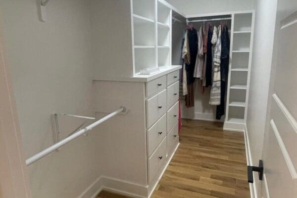 Walk-in closet featuring built-in shelves, a dresser, and hanging space for clothes, showcasing modern design and organized storage solutions.