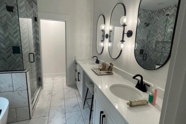 Modern bathroom featuring dual sinks with round mirrors, stylish lighting, and a glass shower, showcasing custom tile work and elegant design elements.