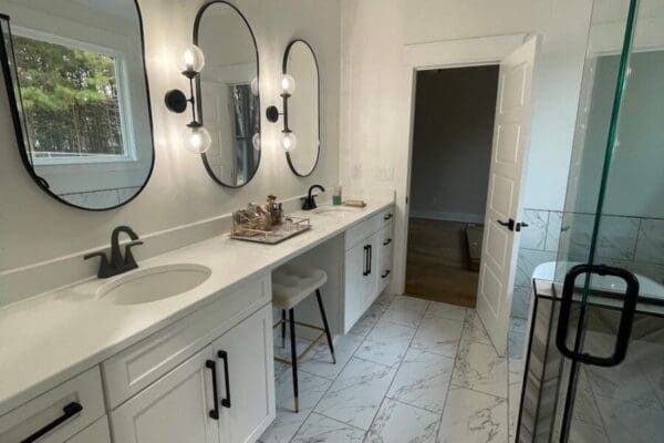 Modern bathroom featuring white cabinetry, dual sinks with circular mirrors, stylish lighting, and a spacious glass shower with elegant tilework.