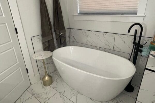 Modern bathroom featuring a freestanding white bathtub, gold accent table, and stylish gray towels, showcasing elegant tile work and contemporary design.