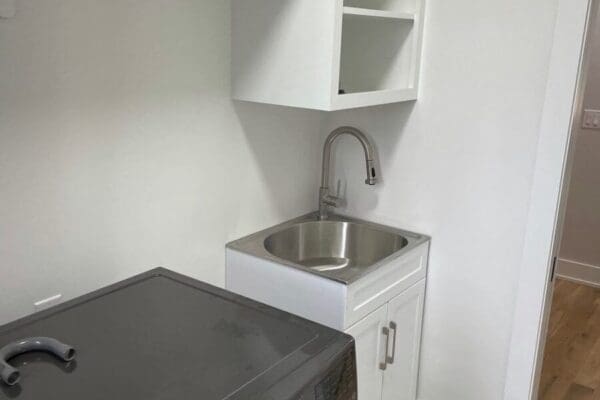 Laundry area with stainless steel sink, modern faucet, and white cabinetry, featuring a washing machine beside it, designed for efficient home functionality.