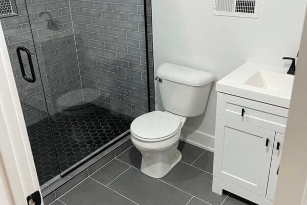 Modern bathroom featuring a glass shower, white toilet, and sleek vanity with white cabinetry and gray tile flooring, highlighting contemporary design elements for custom home aesthetics.