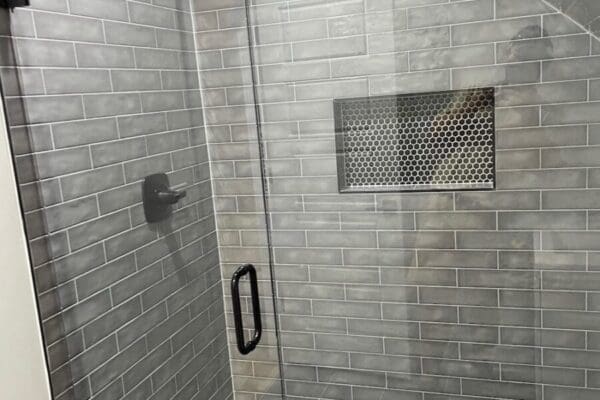 Modern shower enclosure featuring gray subway tile, sleek glass door, and integrated niche for toiletries, showcasing custom design elements for a stylish bathroom.