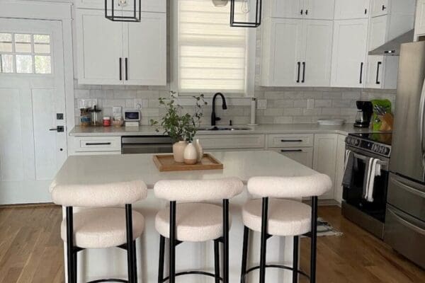 Modern kitchen with white cabinetry, quartz countertops, large center island, and stylish bar stools, featuring warm hardwood floors and contemporary lighting, ideal for custom home design inspiration.